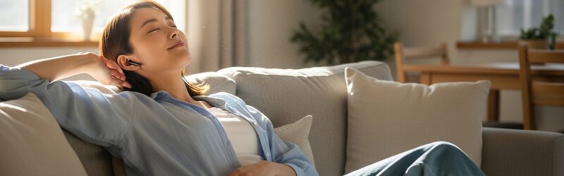 リビングで「聴く読書」をオーディブルで楽しむ女性。本を持たず、プロのナレーターが読み上げる本を聴くメリットを知ってリラックスしている