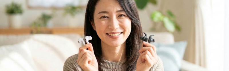 Bluetoothバージョンの違う2つのイヤホンをもっている笑顔の女性。