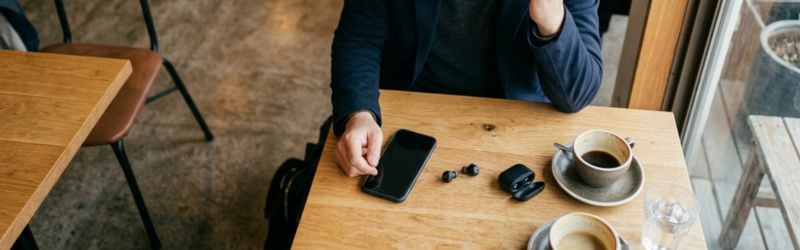 カフェで動かなくなったワイヤレスイヤホンを眺めて茫然とする男性。